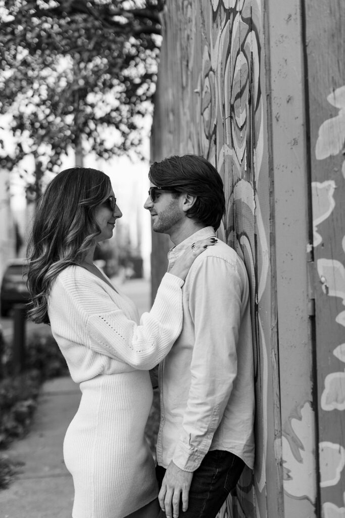 couple leaning against wall and smiling at each other