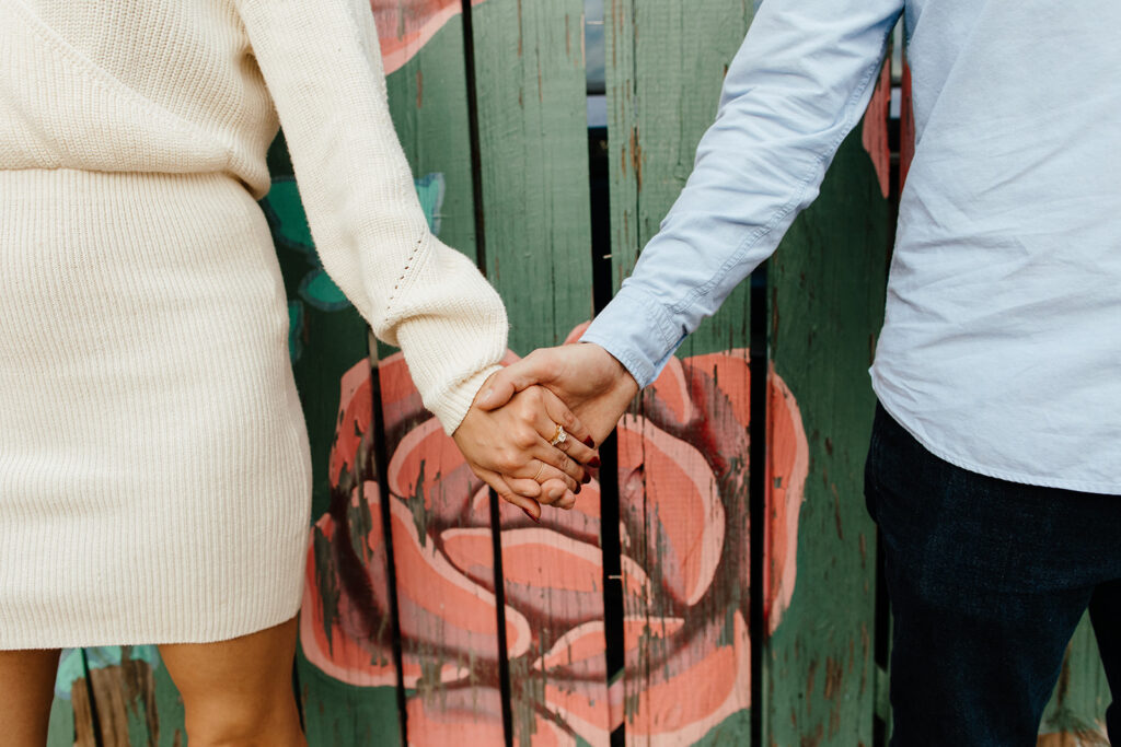 couple holding hands in front of colorful wall for engagement photoshoot